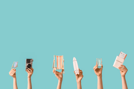 Female hands holding mini deck chairs with surfboard, camera and passport on blue backgroundの写真素材