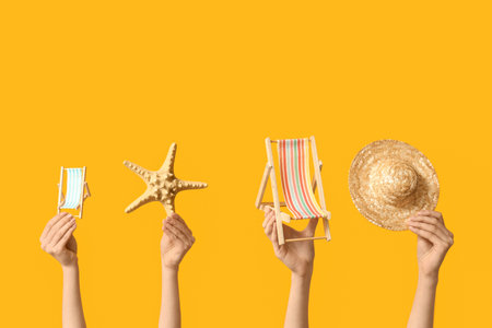 Female hands holding mini deck chairs with hat and starfish on yellow backgroundの写真素材
