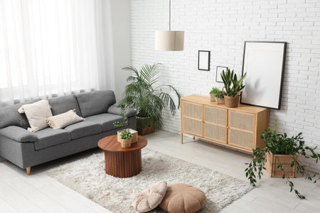 Interior of stylish living room with gray sofa, wooden cabinet, coffee table and houseplants in...