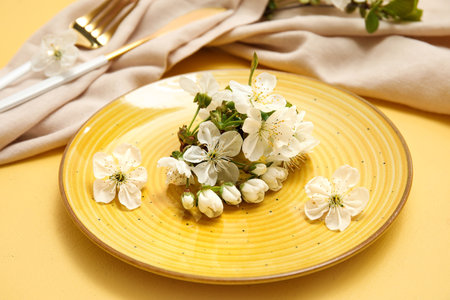 Beautiful table setting with blooming branch on yellow background, closeupの写真素材