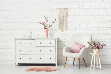 Interior of stylish living room with white armchair, blooming tree branches on dresser and coffee...