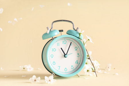 Alarm clock and flowers on beige background. Spring time