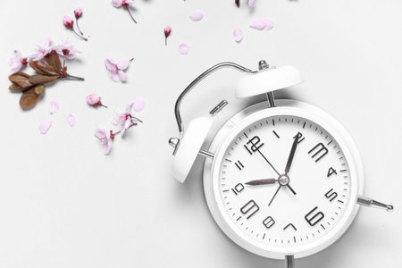 Alarm clock and flowers on gray background. Spring time