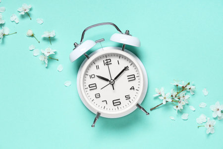 Alarm clock and flowers on turquoise background. Spring time