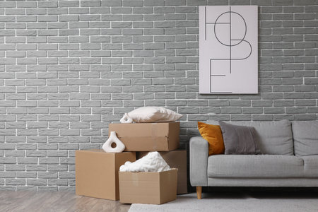 Stylish poster and sofa with cardboard boxes in room on moving day