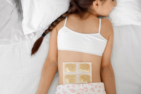 Ill girl with mustard plaster on her back lying in bedroom, top viewの写真素材