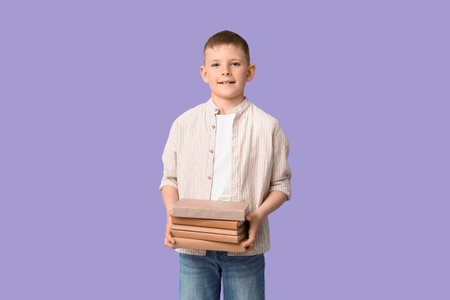 Cute little boy with stack of books on lilac backgroundの写真素材