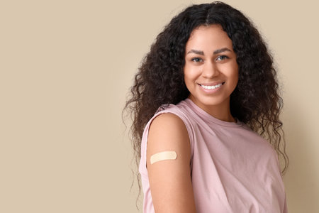 Young African-American woman with medical patch after vaccination on beige background, closeupの写真素材