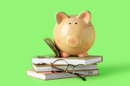 Piggy bank with dollar banknotes, coins, books and eyeglasses on green backgroundの写真素材