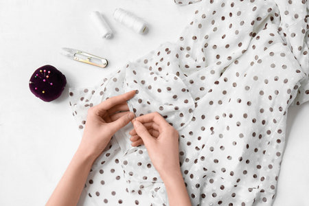 Woman sewing stylish dress on light background