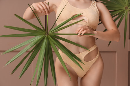 Young woman in stylish swimsuit with palm leaves on brown backgroundの写真素材