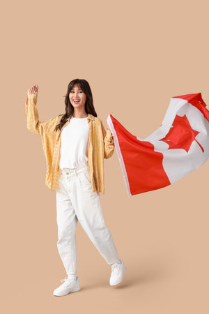 Young woman with waving flag of Canada on beige backgroundの写真素材