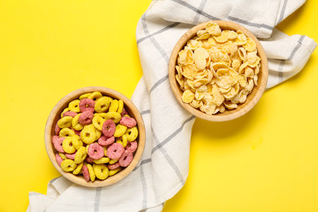 Wooden bowls with cornflakes and color cereal rings on yellow backgroundの写真素材