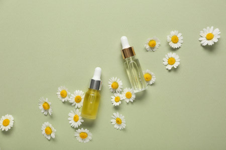 Bottles of cosmetic products with chamomile flowers on green backgroundの写真素材