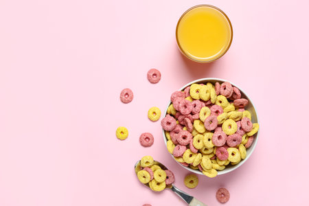 Bowl of tasty color cereal rings and glass of juice on pink backgroundの写真素材