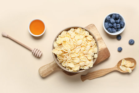 Composition with bowls of tasty cornflakes, blueberry and honey on beige backgroundの写真素材