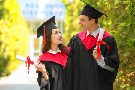 Couple of graduating students with diplomas hugging outdoorsの写真素材