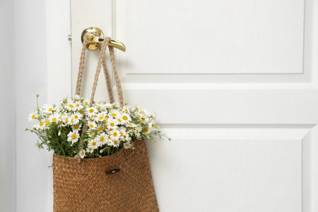 Wicker bag with chamomiles hanging on door in roomの写真素材