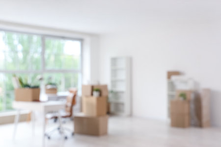 Blurred view of light office with workplace, shelf units and cardboard boxes on moving dayの写真素材