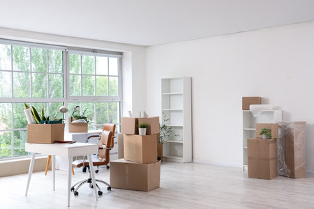 Interior of light office with workplace, shelf units and cardboard boxes on moving dayの写真素材