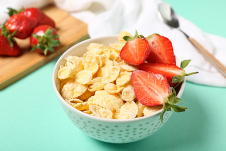 Bowl of tasty cornflakes and strawberry on turquoise background, closeupの写真素材