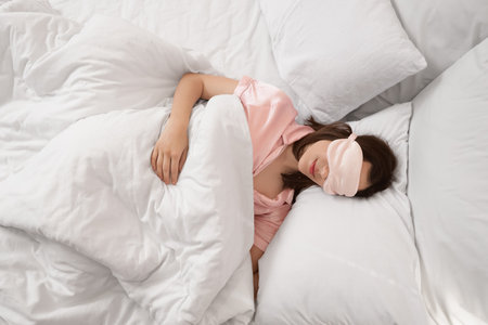 Young woman with mask sleeping on pillows in bedroom, top viewの写真素材
