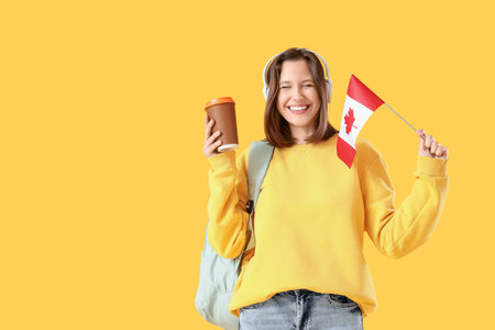 Female student in headphones with flag of Canada and coffee cup on yellow backgroundの写真素材