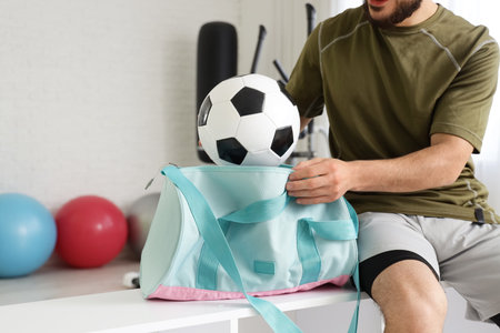 Young man taking soccer ball from sports bag at gymの写真素材