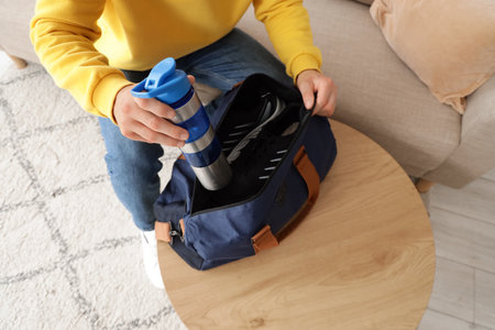 Young man with water bottle from sports bag at home, top viewの写真素材
