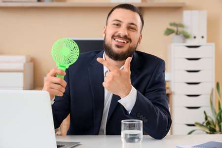 Young businessman pointing at mini fan in officeの写真素材