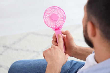 Young man turning on mini fan at home, closeup