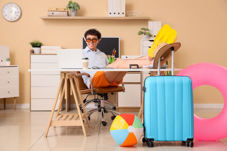Young businessman with cocktail and flippers using laptop in office. Summer vacationの写真素材