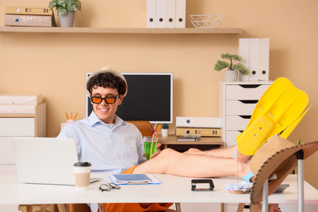 Young businessman with cocktail and flippers using laptop in office. Summer vacationの写真素材