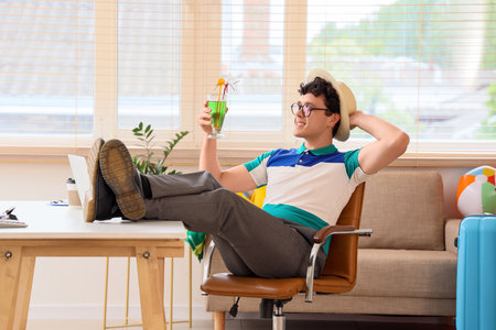 Young businessman with cocktail waiting for summer vacation at table in officeの写真素材