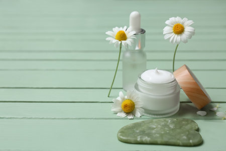 Different chamomile cosmetic products with guasha tool and flowers on green wooden backgroundの写真素材