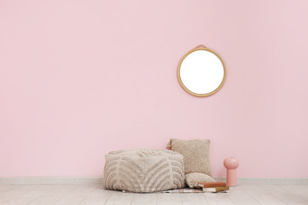Pouf, cushions on floor and round mirror on pink wall in roomの写真素材