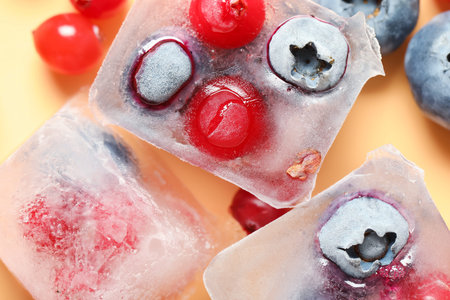 Frozen blueberries and cranberries in ice cubes on orange backgroundの写真素材