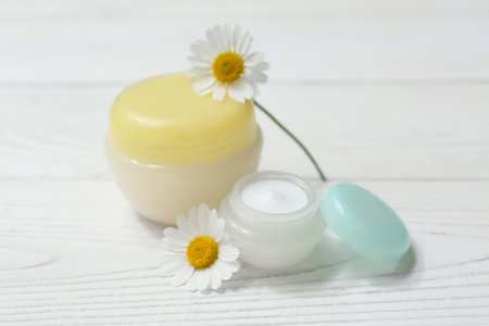 Jars of chamomile cosmetic cream and flowers on white wooden backgroundの写真素材