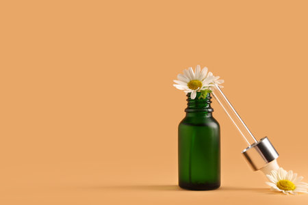 Bottle of chamomile cosmetic oil and flowers on brown backgroundの写真素材