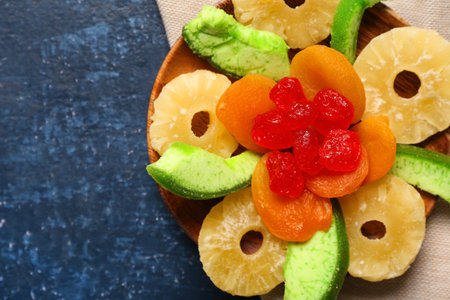 Wooden plate with different candied fruits on blue background