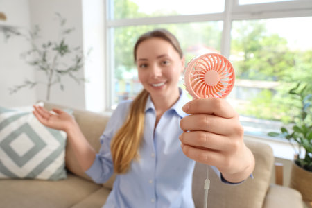 Young woman with mini fan at home, closeupの写真素材
