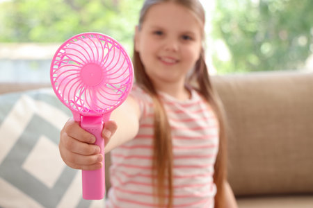 Cute girl with mini fan sitting on sofa at home, closeupの写真素材