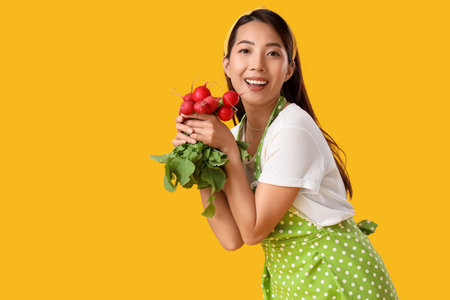 Happy young Asian housewife with ripe radish on yellow backgroundの写真素材