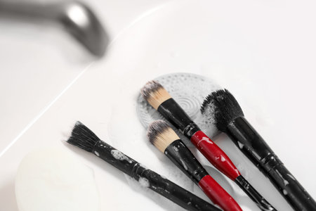 Makeup brushes with cleaning tool and soap in sink, closeup