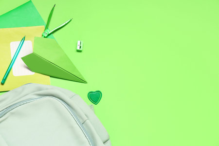 Composition with paper airplane, backpack and school stationery on green background
