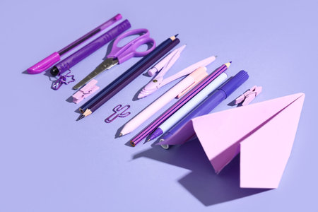 Composition with paper airplane and different school stationery on lilac background, closeup