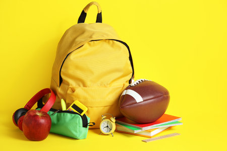 Backpack, school supplies and sports equipment on yellow backgroundの写真素材