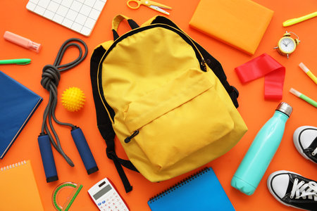 Composition with backpack, school supplies and sports equipment on orange background