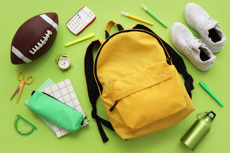 Composition with backpack, school supplies and sports equipment on green background