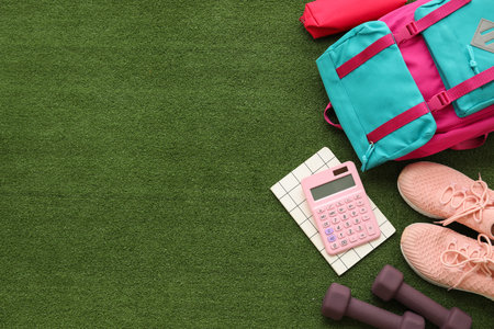 Composition with backpack, calculator and sports equipment on green grass backgroundの写真素材